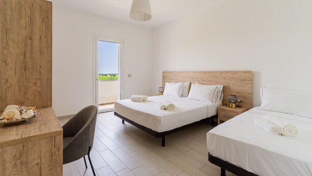 Ein Hotelzimmer mit zwei Betten, einem Schreibtisch, einem Stuhl, einem Holz-Kopfende, einem Nachttisch mit Lampe und Blick ins Freie.