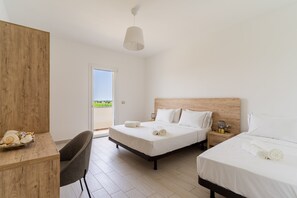 A hotel room with two beds, a desk, a chair, a wooden headboard, a bedside table with a lamp, and a view of the outdoors.