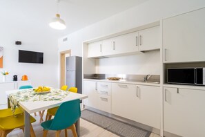 A modern kitchen with white cabinets, a microwave, and a sink. There is a dining table with chairs and a bowl of lemons.