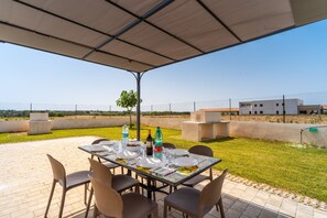 Eine Terrassensitzgelegenheit im Freien mit einem für das Essen gedeckten Tisch, umgeben von Stühlen und Blick auf ein Gebäude im Hintergrund.