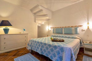 Quarto com cama, mesa de cabeceira, abajur e luminária na parede.