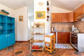 Uma cozinha com armários de madeira, uma estante azul, uma pequena mesa com uma tigela e um tapete xadrez.