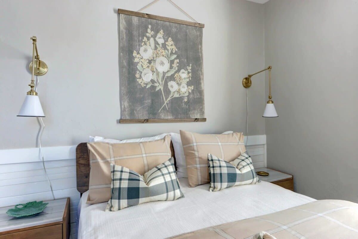Un dormitorio con una cama, dos mesitas de noche, una lámpara de pared y una obra de arte floral.