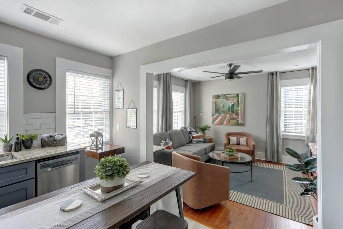 A modern living room with a sofa, armchair, and coffee table. There is a kitchen area with a countertop and a dining table.