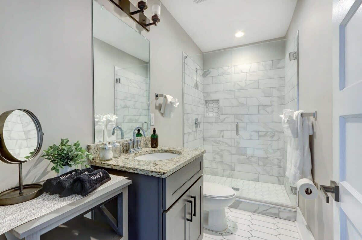 A modern bathroom with a double sink, a large mirror, a shower, and a toilet.