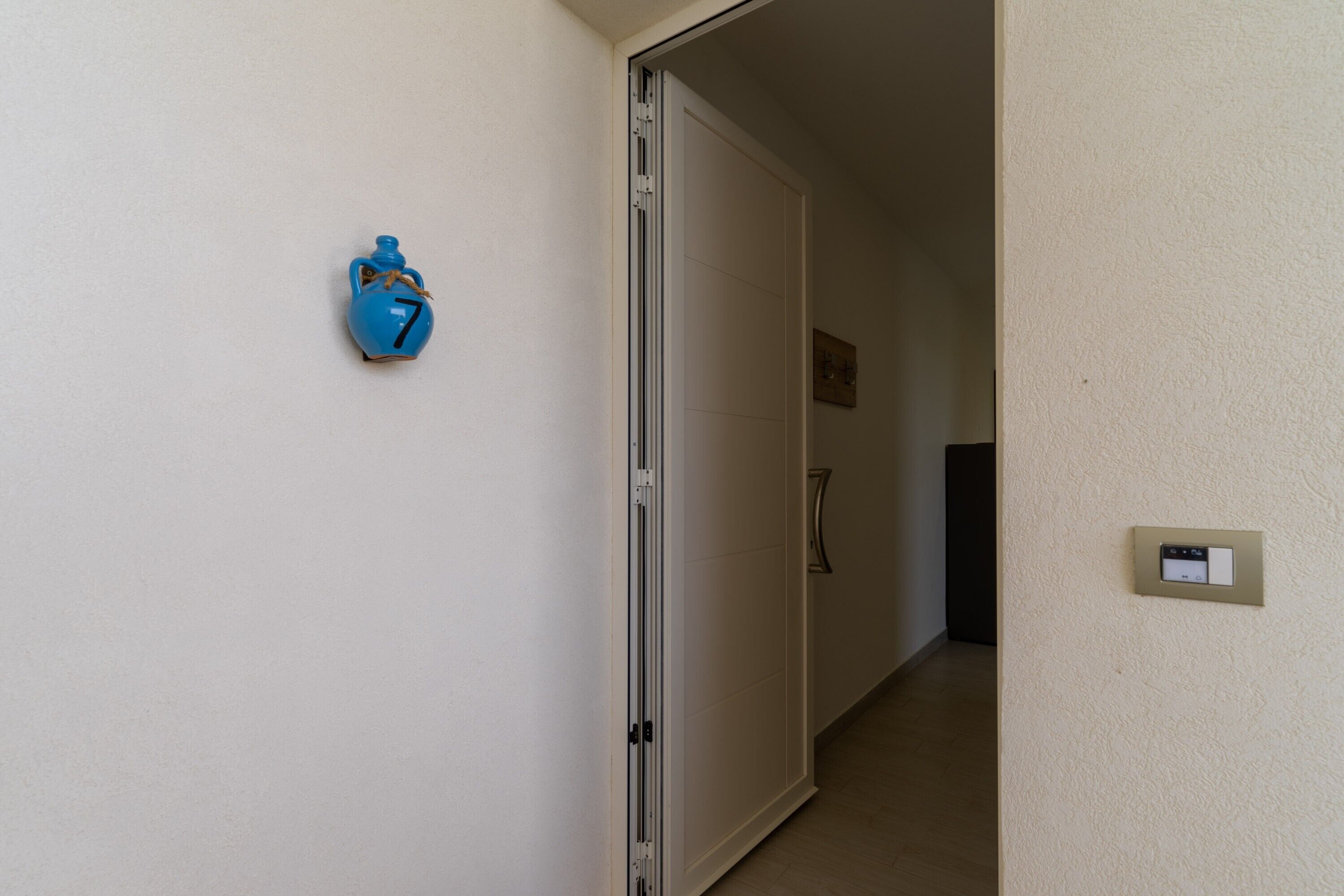 Un couloir avec une porte fermée, un interrupteur fixé au mur et un objet bleu portant un numéro.
