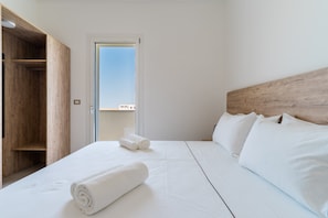 Una camera d'albergo con un armadio in legno, un letto con lenzuola bianche e vista attraverso una porta.