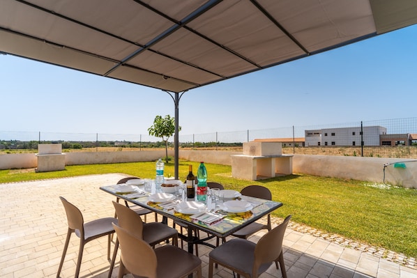 Une terrasse extérieure avec une table dressée pour le repas, entourée de chaises, et une vue sur un bâtiment en arrière-plan.
