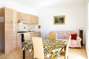Une cuisine compacte avec des meubles en bois, une table à manger recouverte d’une nappe à motifs de tournesols et un canapé avec un revêtement à motifs.