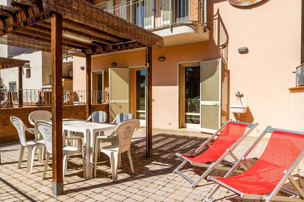 A patio with a table and chairs, a covered area, and two red lounge chairs.
