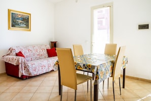 Un coin repas avec une table et des chaises, un canapé recouvert d’un tissu à motifs et un tableau accroché au mur.