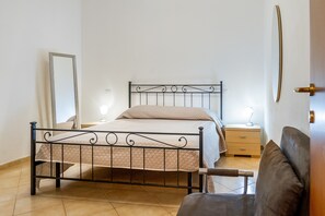 A bedroom with a metal bed frame, a bedside table with a lamp, a dresser, and a chair. - Holiday Apartment "Acqua" with Sea View & Private Garden (Follonica)