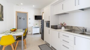 A modern kitchen with white cabinets, a stainless steel sink, and a dining area with a table and chairs.