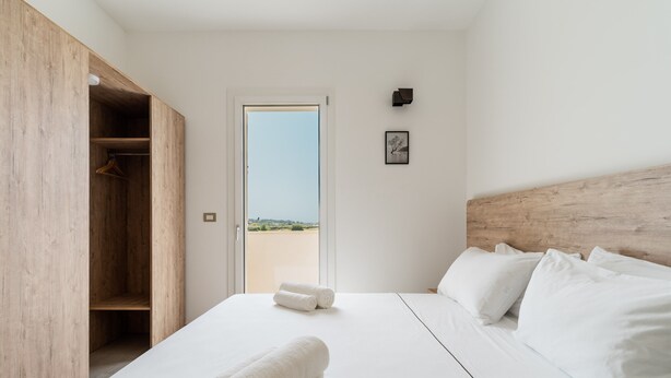 A bedroom with a bed, a wooden wardrobe, a door leading outside, and a small framed picture on the wall.