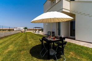 Une terrasse extérieure moderne, dotée d’une table et de chaises, d’un grand parasol et d’une pelouse bien entretenue.