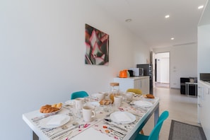 Un espace repas moderne avec une table dressée pour quatre personnes, une machine à café et une cuisine en arrière-plan.