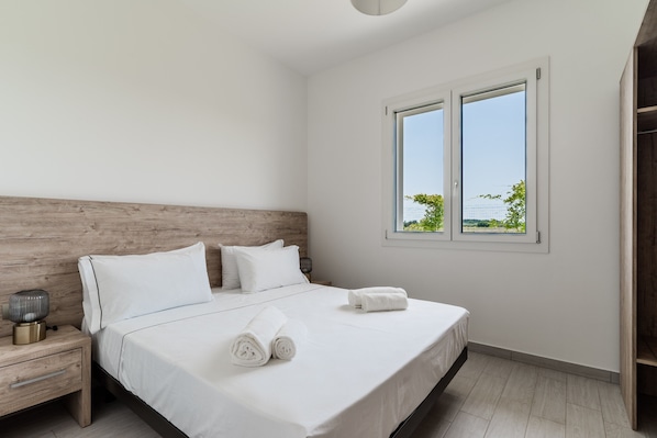 Une chambre à coucher avec une tête de lit en bois, un lit recouvert de draps blancs, une lampe de chevet et une fenêtre donnant sur un paysage verdoyant.