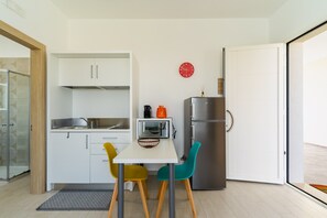 A compact kitchen with white cabinets, a stainless steel refrigerator, a microwave, and a small orange kettle.