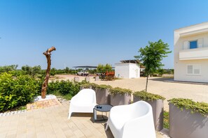 A patio with white chairs and a table, a tree sculpture, and a building with a white facade.