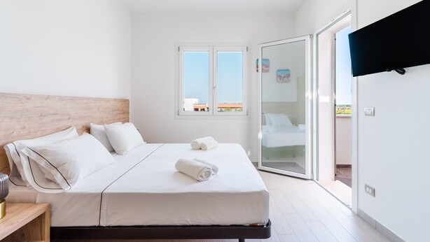 Een slaapkamer met een bed, nachtkastje, raam en een schuifdeur naar buiten.