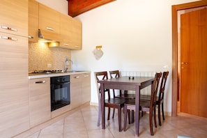 Una cocina con armarios de madera, estufa, horno, mesa de comedor con sillas y una puerta de madera.