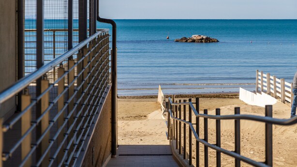 A beach view from a building with a metal railing, a sandy beach, and a rocky outcrop in the water. - Holiday Apartment 'Aria' close to the Beach with Shared Terrace & Balcony (Follonica)