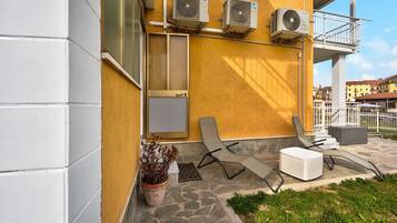 A building with air conditioning units, a balcony, a potted plant, and outdoor seating.