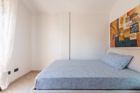 Ein Schlafzimmer mit einem Bett, einem Bild an der Wand und einem Fenster mit Vorhängen.