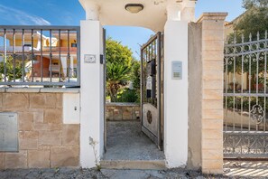 Ingresso recintato a un edificio con muro in pietra, cancello metallico e cielo sereno.