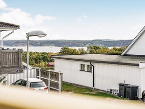 A white mobile home with a sloped roof, a fenced yard, and a view of a body of water and hills in the background.