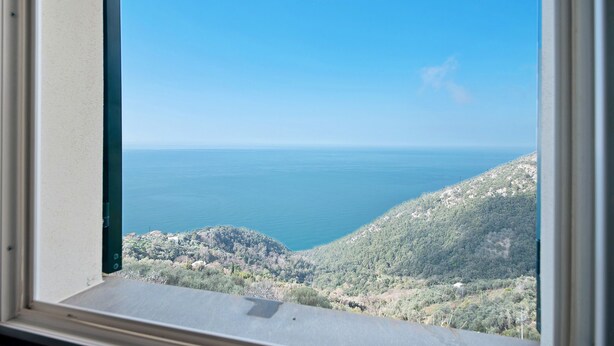 Vista desde una ventana a un paisaje costero con cielo despejado, una masa de agua y terreno montañoso.