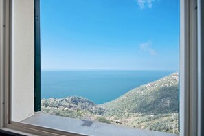 A window view of a coastal landscape with a clear sky, a body of water, and a hilly terrain.