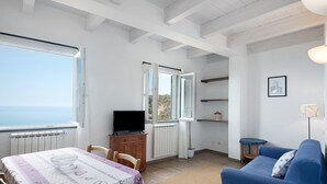 Una habitación con una mesa de comedor, un sofá azul, una televisión y vistas al mar.