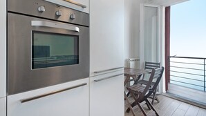 Una cocina moderna con horno integrado, un comedor con mesa y sillas, y un balcón con vistas.