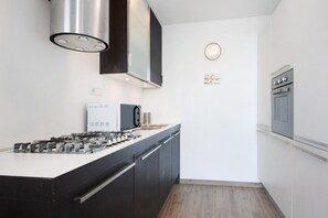 A modern kitchen with a built-in stove, microwave, and oven, with dark cabinetry and a wooden floor.