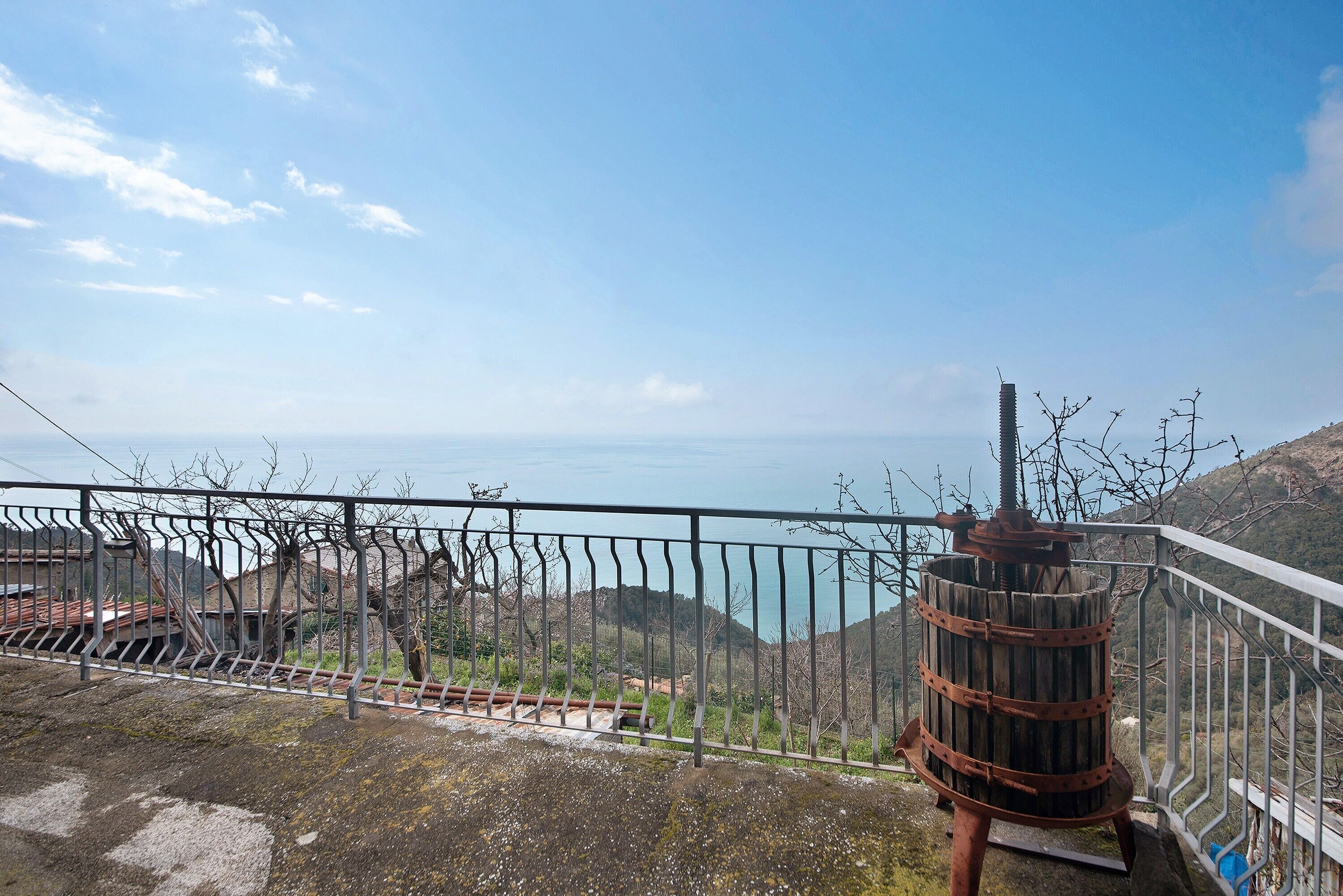 Ein Balkon mit Metallgeländer, der auf eine gebirgige Landschaft und ein Gewässer blickt.