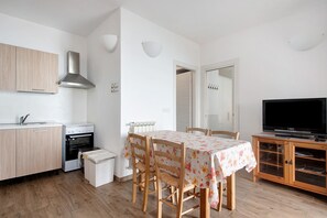 A compact kitchen with wooden cabinets, a stove, and a dining area with a table and chairs.