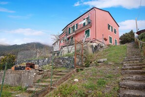 A pink building with a balcony, a stone staircase, and a fence.