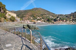 A coastal town with a stone walkway, a mountain in the background, and a beach.