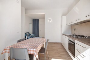A compact kitchen with white cabinets, a dining table with a checkered tablecloth, and a separate dining area with chairs.