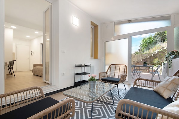 A modern living room with a glass coffee table, wicker furniture, and a view of a garden. - Holiday Home "Moneglia Monte" near the Sea with Private Garden and Wi-Fi (Moneglia)