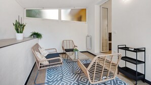 A small balcony with wicker furniture, a potted plant, and a black metal shelf.