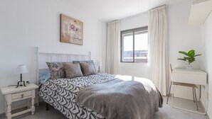 Camera da letto con letto, comodino, lampada, tende, finestra e una scrivania con una pianta.