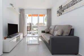 Una sala de estar moderna con un televisor de pantalla plana, un sofá y una mesa de centro de vidrio.