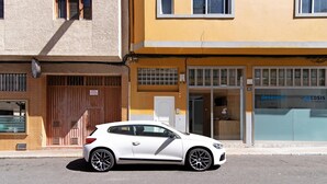 En hvid bil parkeret foran en bygning med en stor garageport og en butiksfacade med skilte.
