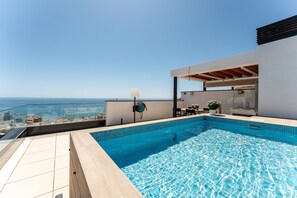 A rooftop swimming pool with a city view, a glass railing, and a modern outdoor seating area.