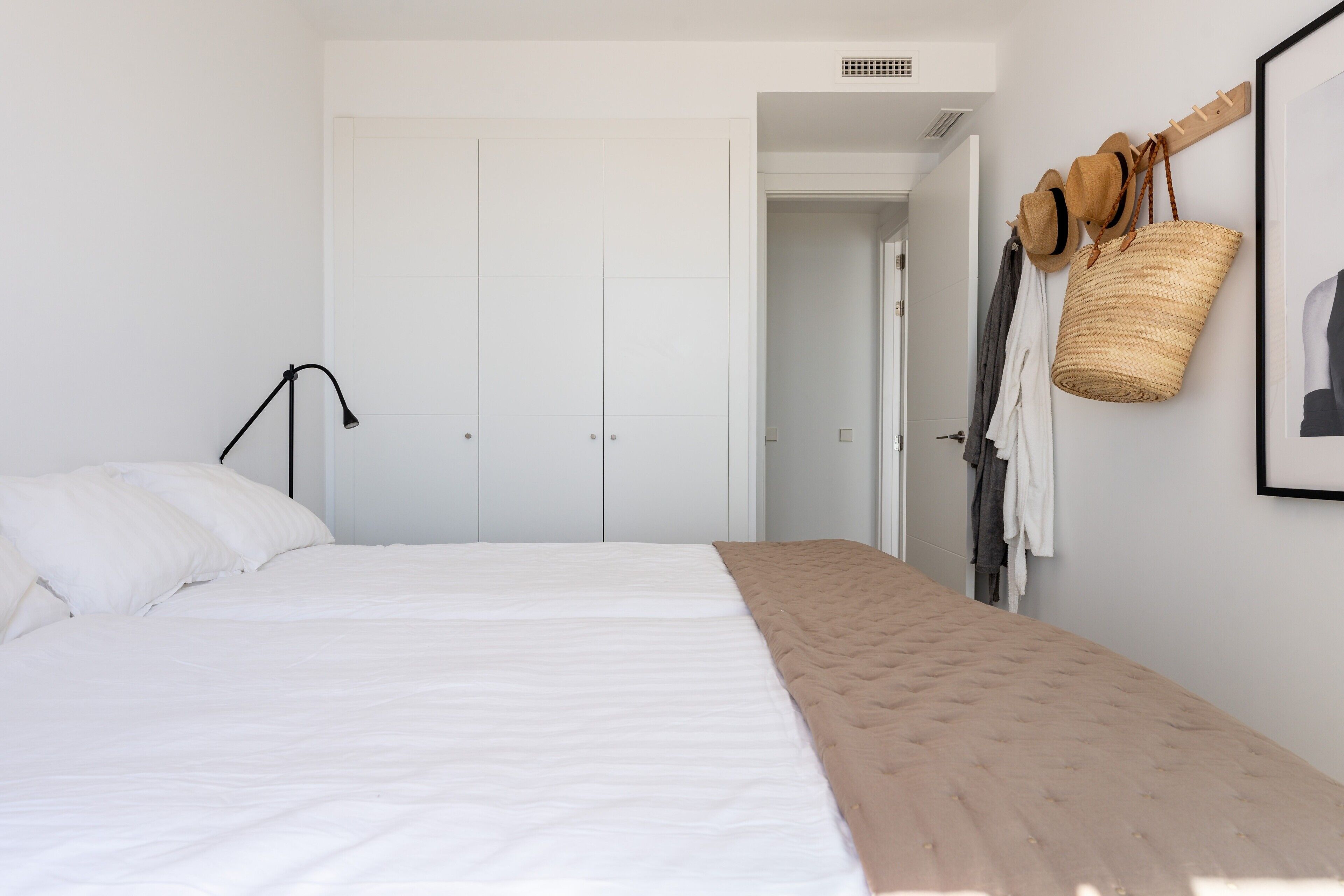A bedroom with a bed, a wardrobe, a lamp, a hat rack, and a basket.