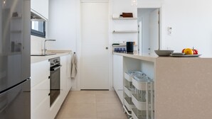 Moderni keittiö, jossa on valkoiset kaapit, sisäänrakennettu uuni, mikroaaltouuni sekä työtaso, jonka päällä on kulho ja hedelmiä.