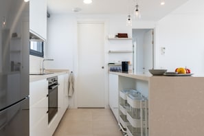 A modern kitchen with white cabinetry, a built-in oven, a microwave, and a countertop with a bowl and fruit.