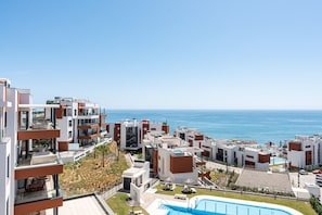 A modern residential complex with multiple buildings, a swimming pool, and a view of the sea.